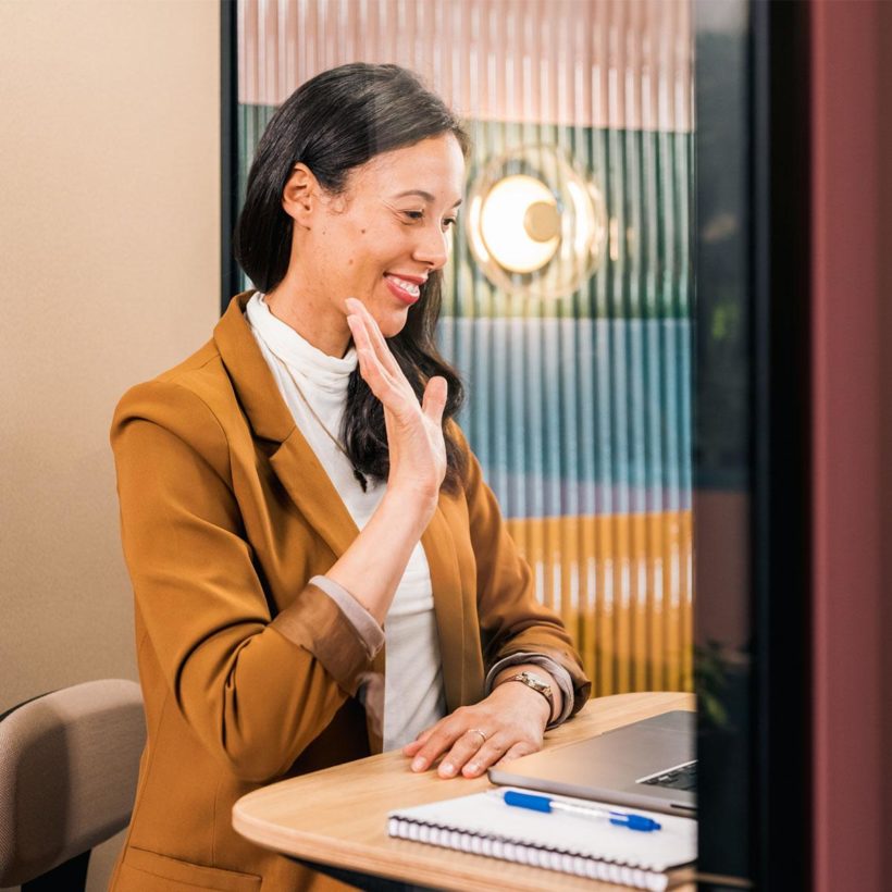 Person waving to their coworkers in a video conference inside a Framery pod