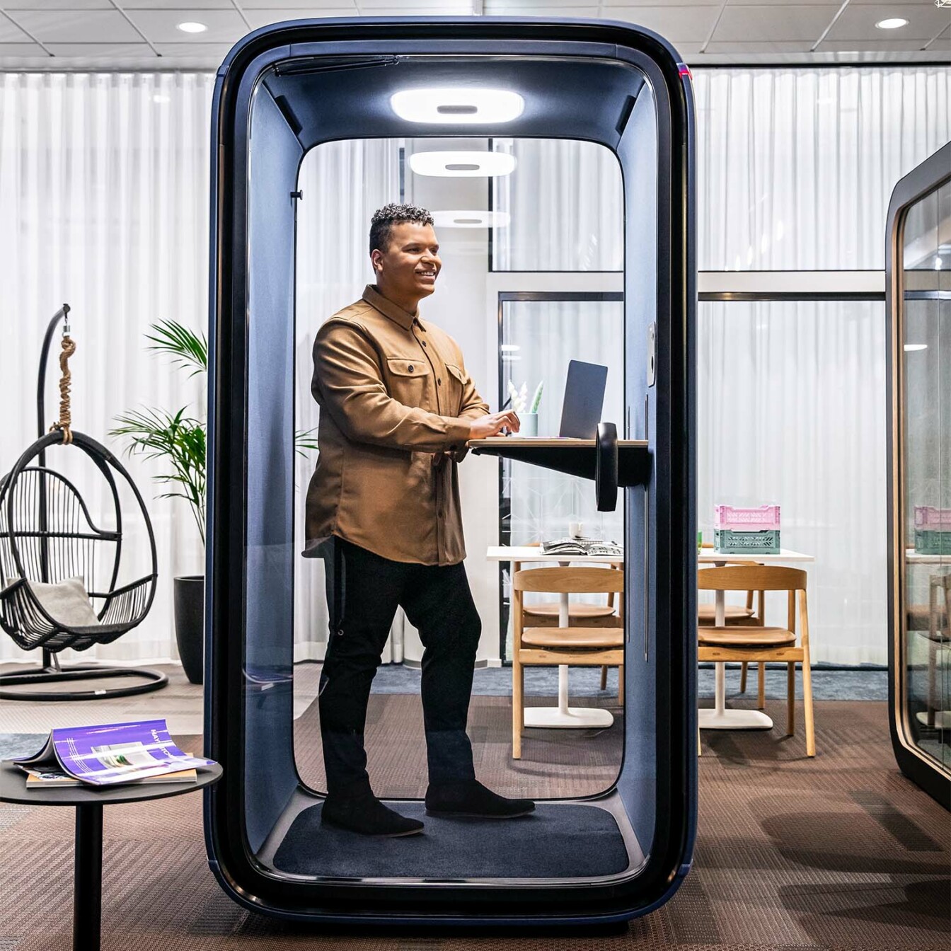 A person smiling and working in a Framery One office pod.
