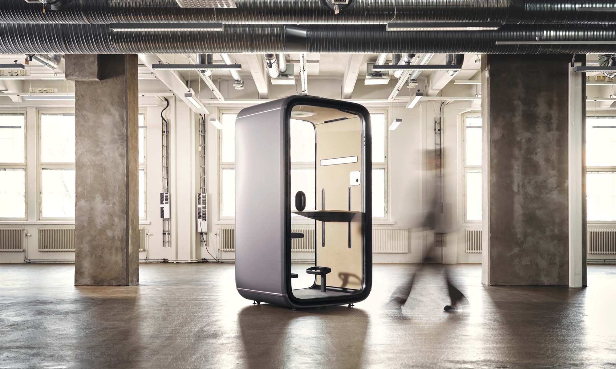 Framery One office pod in an open space with a person walking towards it.